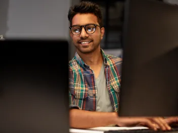 Young man with glasses smiling and looking at a computer