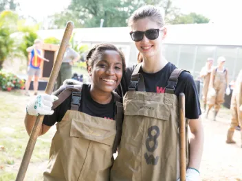 Two girls in bibs and digging equipment outdoors