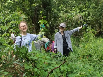 two volunteers hold up invasive plants they are collecting as part of an NPLD event