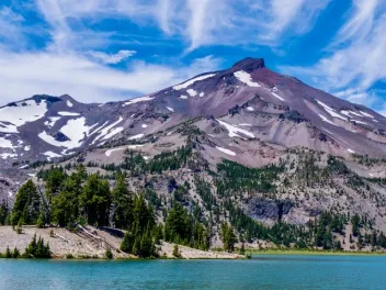 small patches of snow sit on the side of a mountain top with exposed dirt