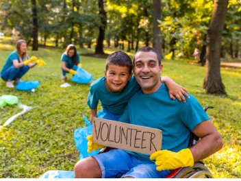 a father and son outdoors holding a sign that says volunteer during a clean up