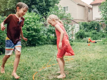 Two children playing with a sprinkler in their backyard.