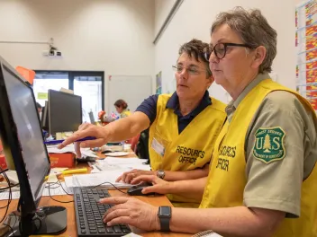 Two women wearing US Forest Service uniforms work together at a desk