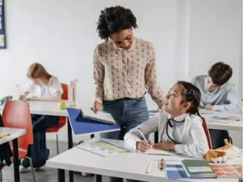 a female teacher speaks with a girl student at her desk