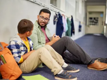 a teacher sits with a student for a discussion in a hallway