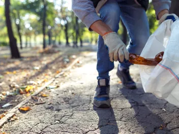 Person putting plastic bottle in garbage bag for national public lands day volunteer clean up event.