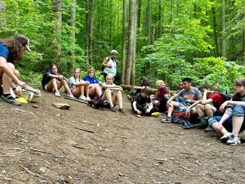 a group of students sits on the forest floor for a Greening STEM outdoor education lesson