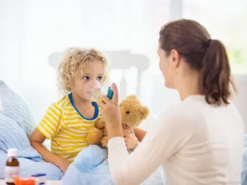a young boy uses an asthma inhaler administered by a parent