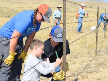a volunteer leader instructors two young volunteers on fence repair
