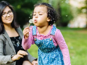 Daughter blowing on a dandelion while her mom watches