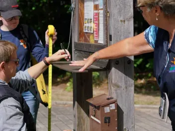 Three people measuring the height of a signing station to ensure accessibility for those in wheelchairs