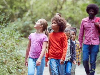 Male teacher walking with students in the forest while they look up at the trees