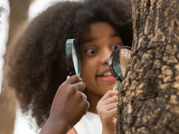 two children holding magnifying glasses and looking at a tree