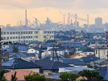 view of rooftops and homes with an industrial center and smokestacks in the distance